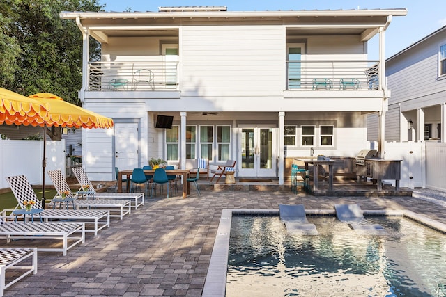 rear view of property with a patio area, a balcony, fence, and french doors