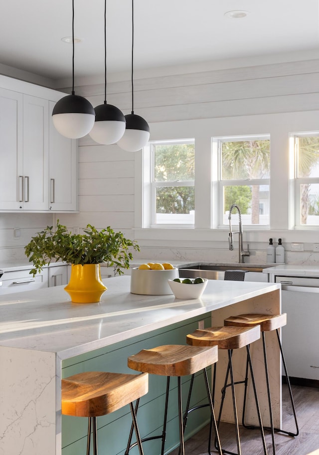 kitchen with decorative light fixtures, dishwasher, a kitchen breakfast bar, white cabinetry, and a sink