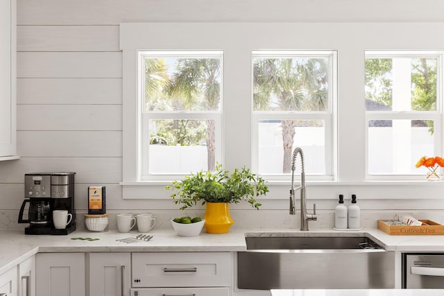 kitchen featuring white cabinetry, light stone counters, a wealth of natural light, and a sink