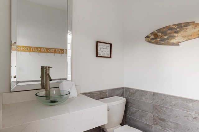 half bathroom featuring a sink, toilet, tile walls, and wainscoting