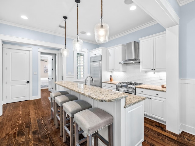 kitchen featuring dark wood-type flooring, high quality appliances, a breakfast bar, crown molding, and wall chimney range hood