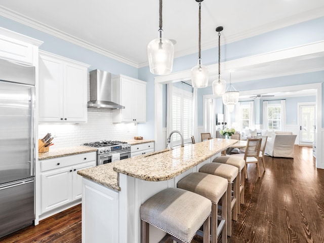 kitchen with high end appliances, ornamental molding, a sink, a kitchen bar, and wall chimney exhaust hood