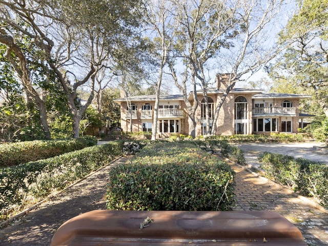 view of front of house featuring a balcony, a chimney, and brick siding