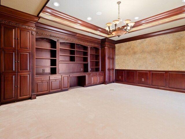 unfurnished living room with light carpet, built in desk, wainscoting, a decorative wall, and crown molding