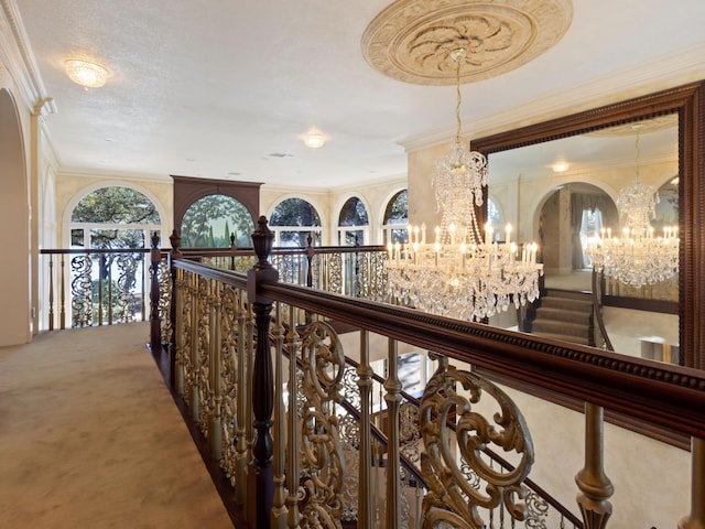 hall with an upstairs landing, carpet floors, a chandelier, and crown molding