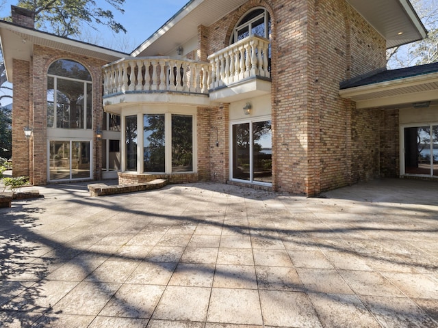 back of property featuring brick siding and a balcony