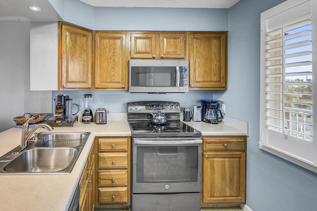 kitchen with brown cabinetry, recessed lighting, a sink, stainless steel appliances, and light countertops