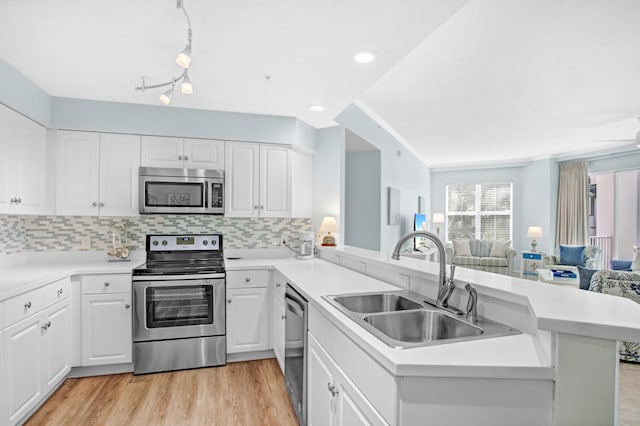 kitchen with a sink, open floor plan, stainless steel appliances, light wood-style floors, and a peninsula