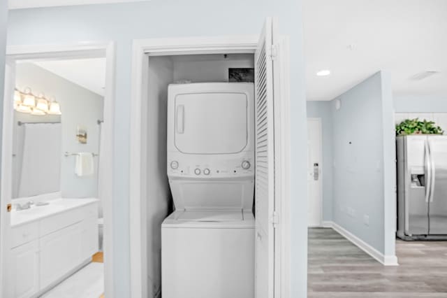 laundry room with baseboards, laundry area, a sink, stacked washer and dryer, and light wood-type flooring