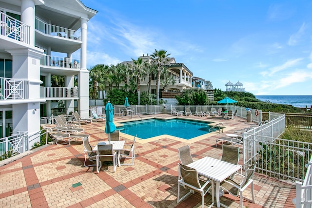 community pool featuring a patio, a water view, and fence