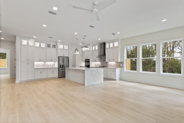 kitchen featuring light wood-style flooring, stainless steel fridge, wall chimney exhaust hood, light countertops, and decorative backsplash