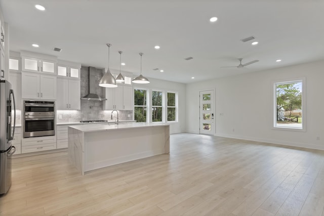 kitchen with visible vents, open floor plan, appliances with stainless steel finishes, wall chimney exhaust hood, and decorative backsplash