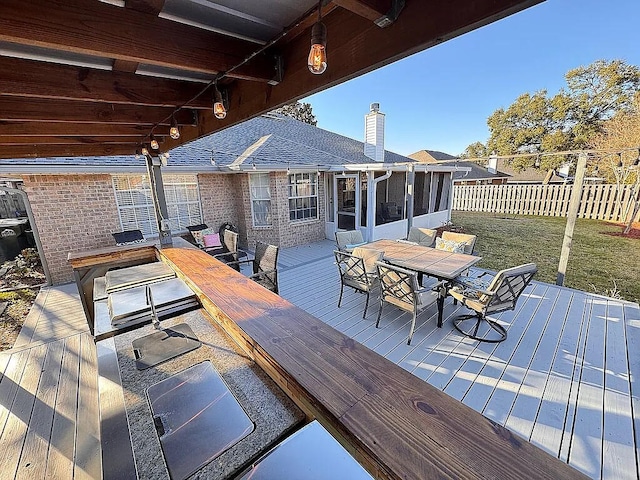 wooden deck with outdoor dining space, fence, a lawn, and a sunroom