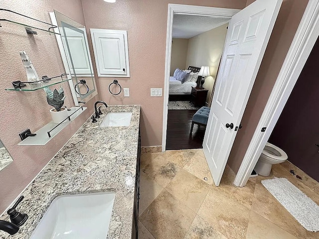 bathroom with ensuite bath, double vanity, toilet, and a sink