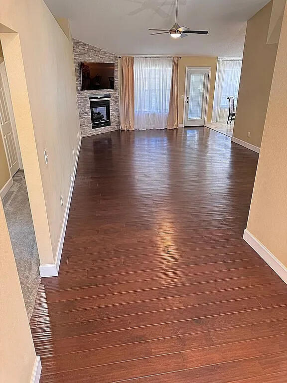 unfurnished living room with a stone fireplace, baseboards, dark wood-type flooring, and a ceiling fan