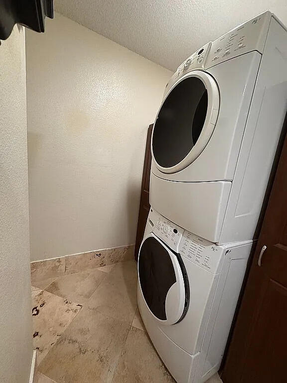 clothes washing area featuring laundry area, a textured ceiling, and stacked washer and dryer