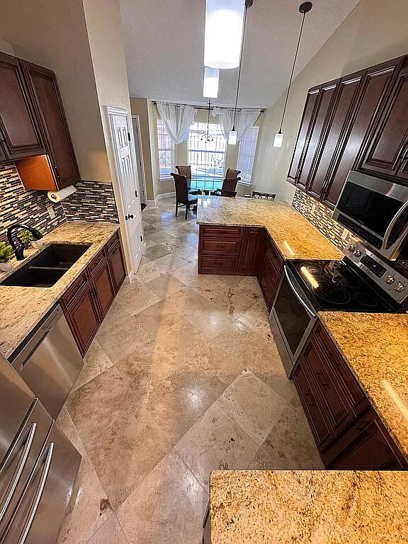 kitchen featuring a sink, light stone counters, backsplash, stainless steel appliances, and a peninsula