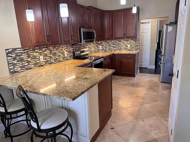 kitchen with tasteful backsplash, appliances with stainless steel finishes, a breakfast bar area, a peninsula, and hanging light fixtures