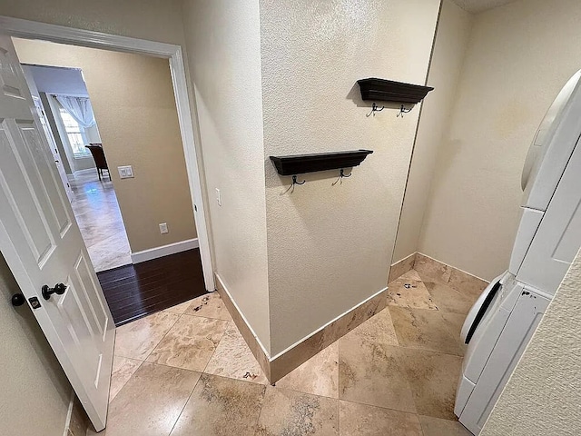 bathroom with stone tile floors, a textured wall, and baseboards