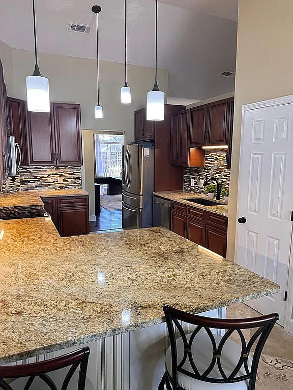 kitchen with visible vents, a peninsula, a sink, decorative backsplash, and appliances with stainless steel finishes