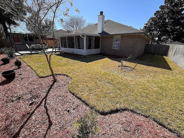 rear view of house with a fenced backyard, a sunroom, a lawn, a patio area, and brick siding