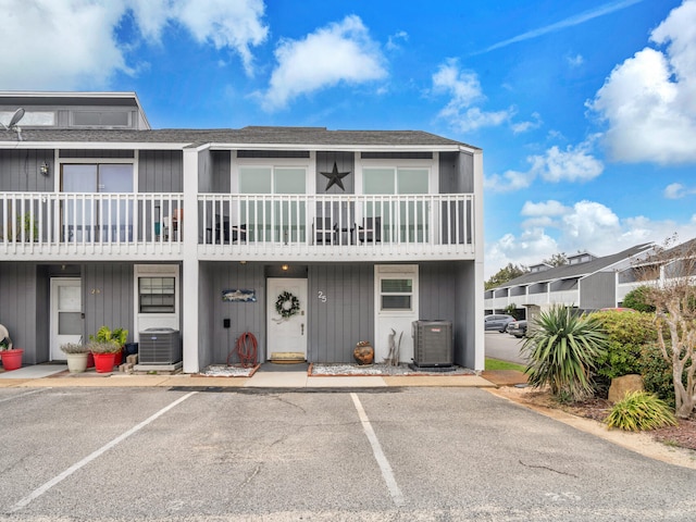 multi unit property featuring central AC unit, roof with shingles, and uncovered parking