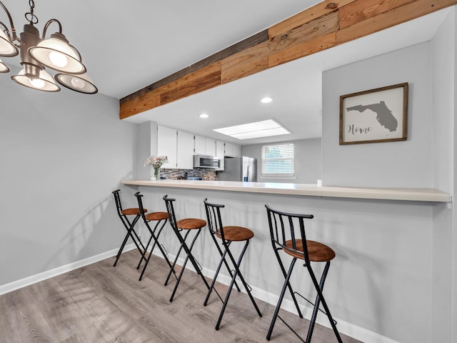 kitchen featuring beamed ceiling, backsplash, light wood-style floors, appliances with stainless steel finishes, and a skylight