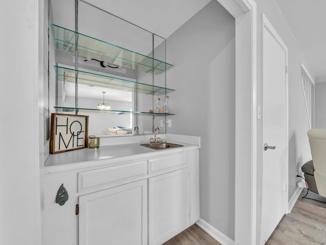 bar featuring light wood finished floors, wet bar, baseboards, and a sink