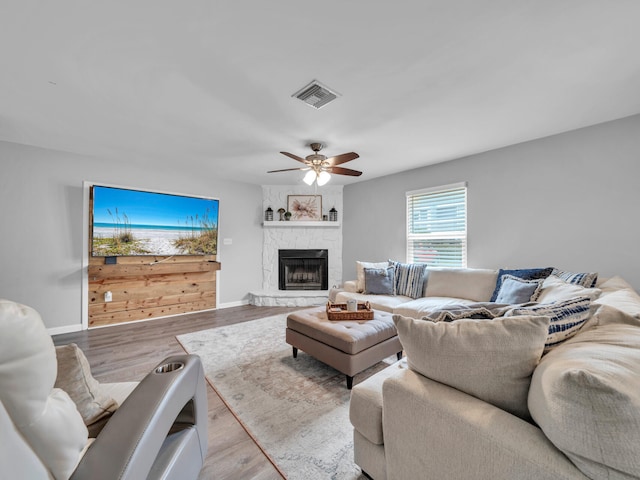 living room with visible vents, baseboards, a fireplace, wood finished floors, and a ceiling fan