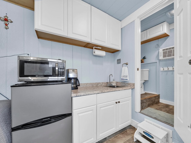 kitchen with an AC wall unit, appliances with stainless steel finishes, white cabinetry, and a sink