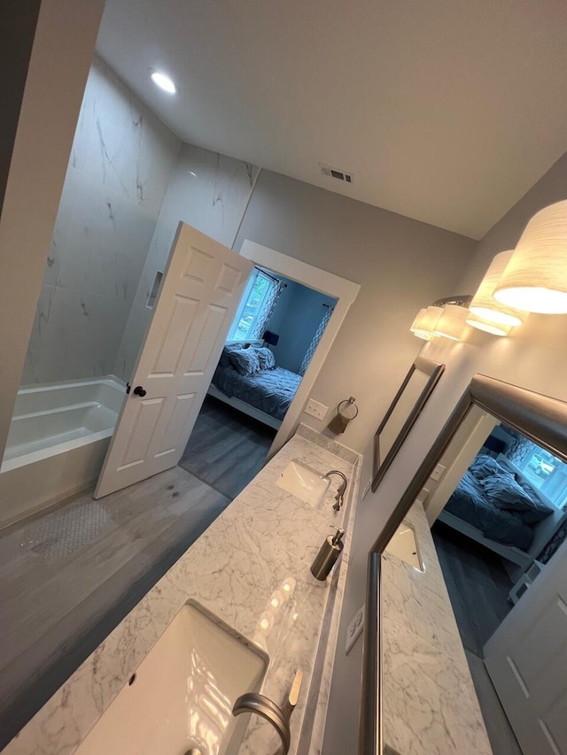 ensuite bathroom featuring visible vents, connected bathroom, double vanity, wood finished floors, and a sink