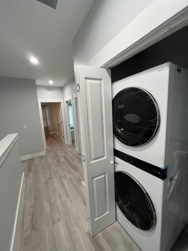 washroom featuring light wood finished floors, visible vents, baseboards, laundry area, and stacked washer and clothes dryer