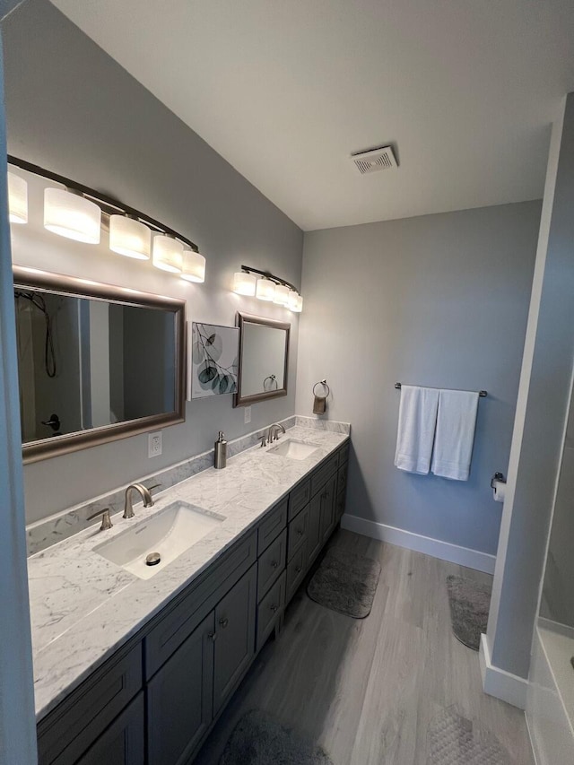 full bath featuring visible vents, baseboards, double vanity, wood finished floors, and a sink