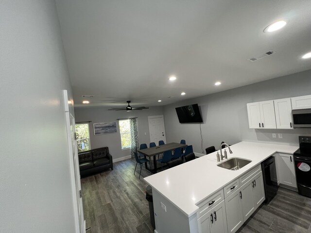 kitchen featuring black appliances, a sink, dark wood finished floors, a peninsula, and light countertops