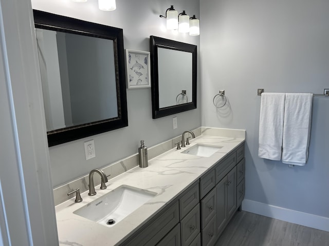 full bath with double vanity, wood finished floors, baseboards, and a sink