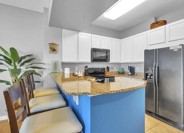 kitchen featuring light stone countertops, a peninsula, black appliances, and white cabinets