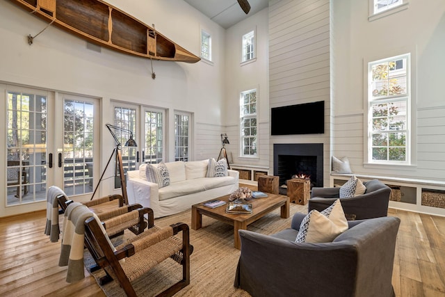 living room featuring light wood-type flooring, french doors, a large fireplace, and a towering ceiling