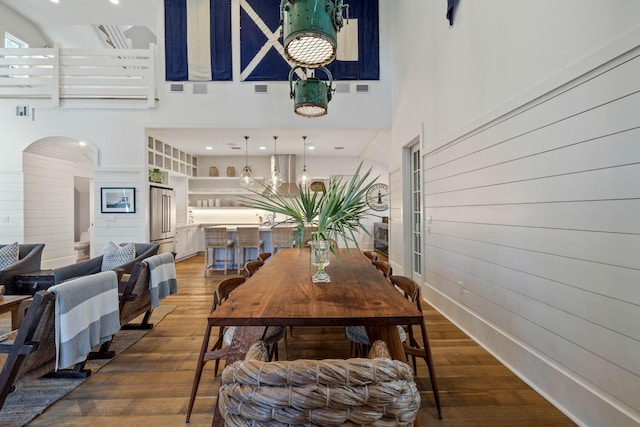 dining space featuring arched walkways, visible vents, a high ceiling, and wood finished floors