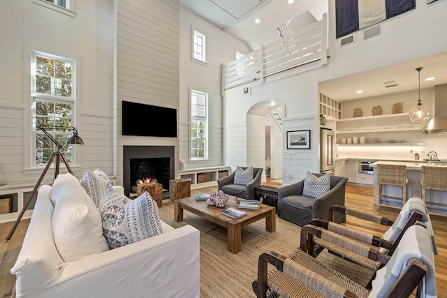 living area featuring a high ceiling, a fireplace, visible vents, and light wood finished floors