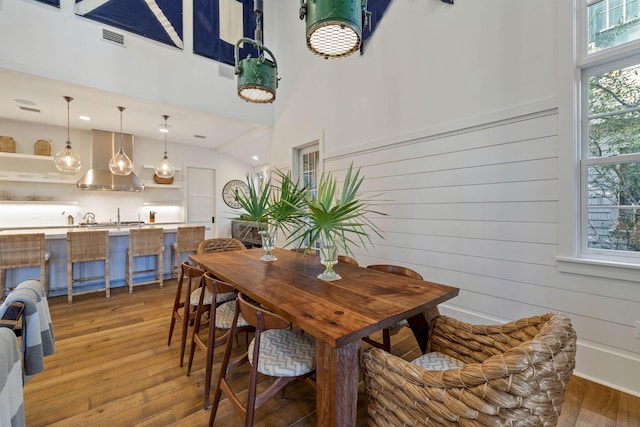 dining space featuring light wood-style floors, visible vents, and a towering ceiling