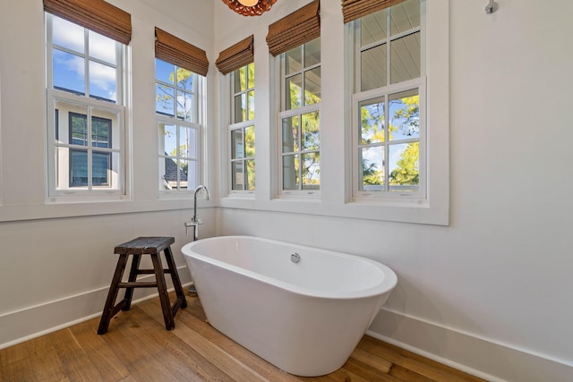 full bath with a freestanding tub, wood finished floors, and baseboards