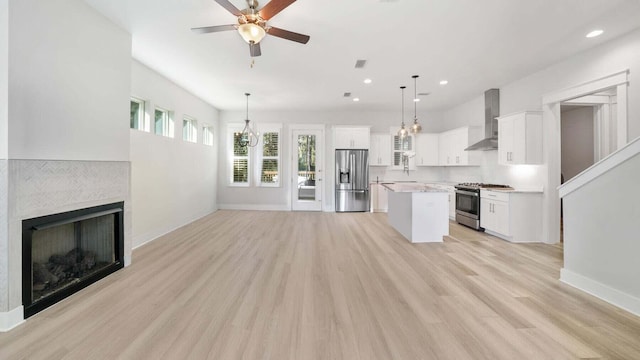 kitchen with open floor plan, a center island, appliances with stainless steel finishes, wall chimney exhaust hood, and a tile fireplace