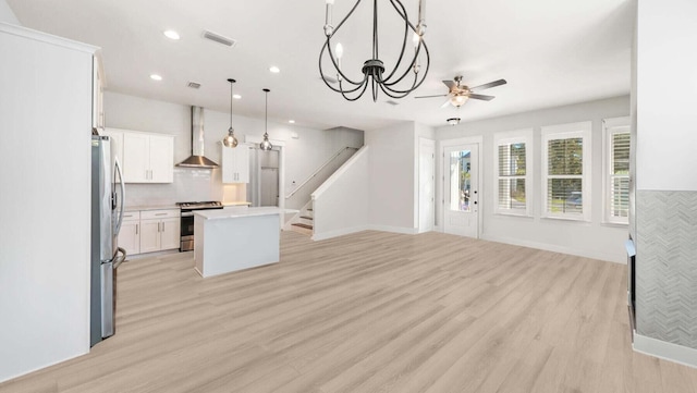 kitchen featuring open floor plan, light wood-style flooring, stainless steel appliances, and wall chimney range hood