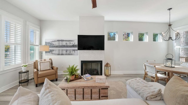 living room featuring wood finished floors, a notable chandelier, a fireplace, and baseboards