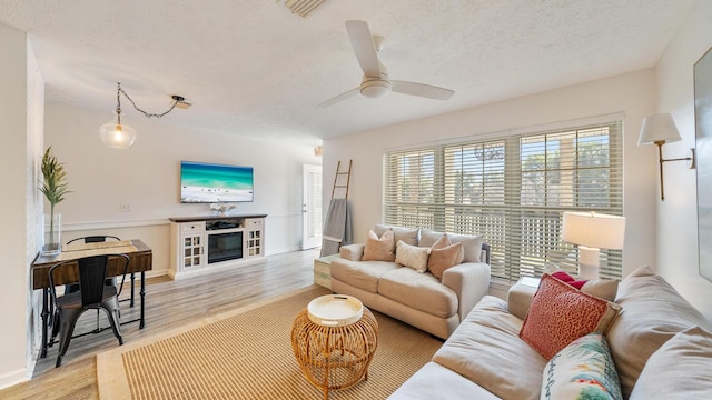 living room with visible vents, ceiling fan, light wood-style flooring, a fireplace, and a textured ceiling