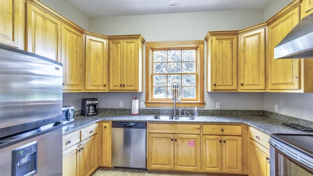 kitchen with appliances with stainless steel finishes, wall chimney exhaust hood, dark stone countertops, and a sink