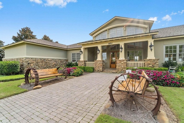 view of front facade with stucco siding, decorative driveway, covered porch, and stone siding