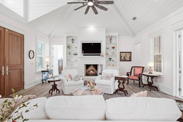 living room with visible vents, built in shelves, a warm lit fireplace, wood finished floors, and baseboards