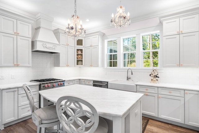 kitchen with high end stove, a chandelier, wood finished floors, custom exhaust hood, and a sink