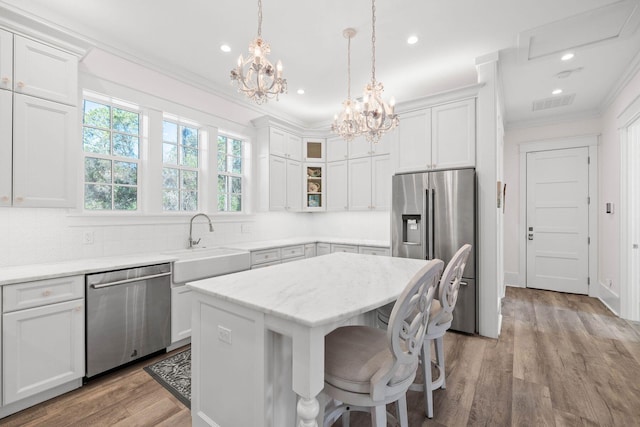 kitchen featuring ornamental molding, a sink, a kitchen island, stainless steel appliances, and glass insert cabinets